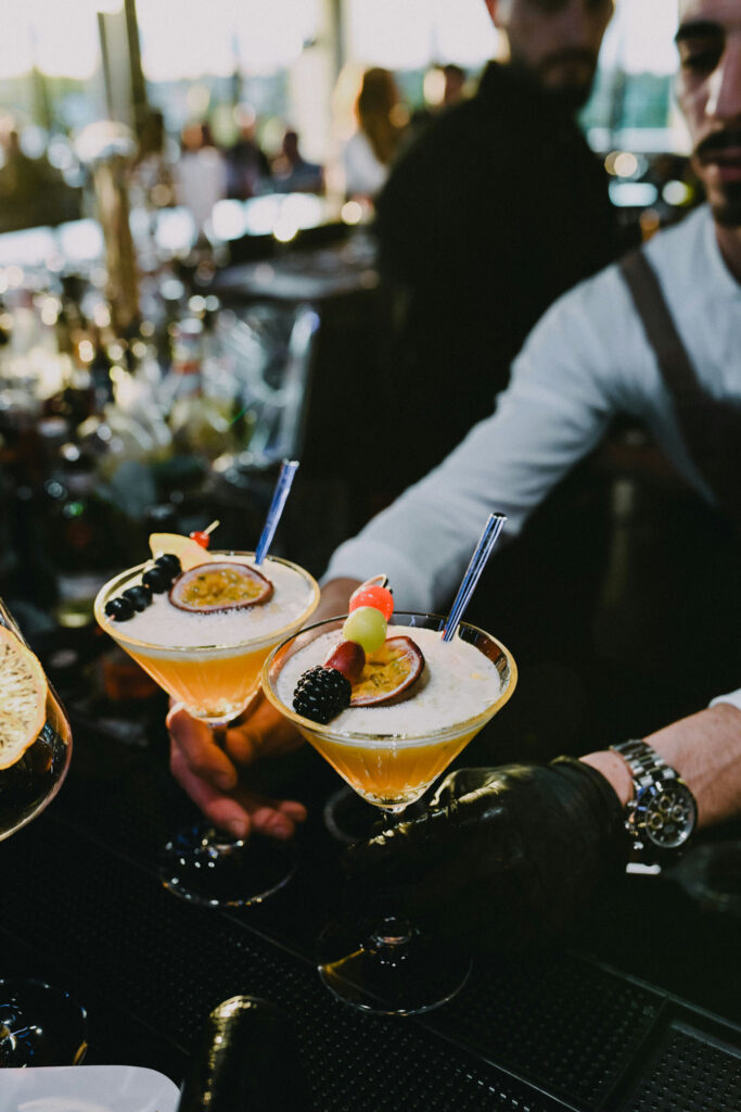Bartender serving two fruit-garnished cocktails at an event