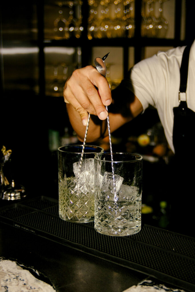 Bartender stirring drinks in crystal glasses filled with ice