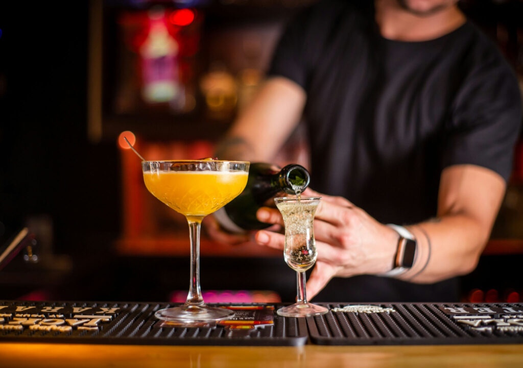 Bartender topping a yellow cocktail with sparkling wine