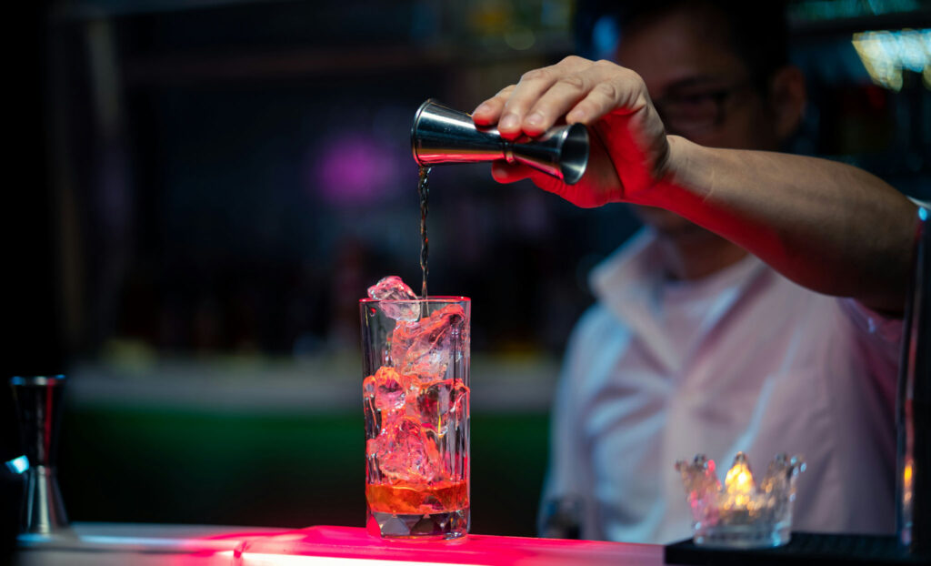 Event bartender measuring liquor into a tall glass over ice