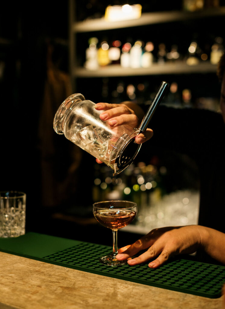 Bartender straining a cocktail into a coupe glass